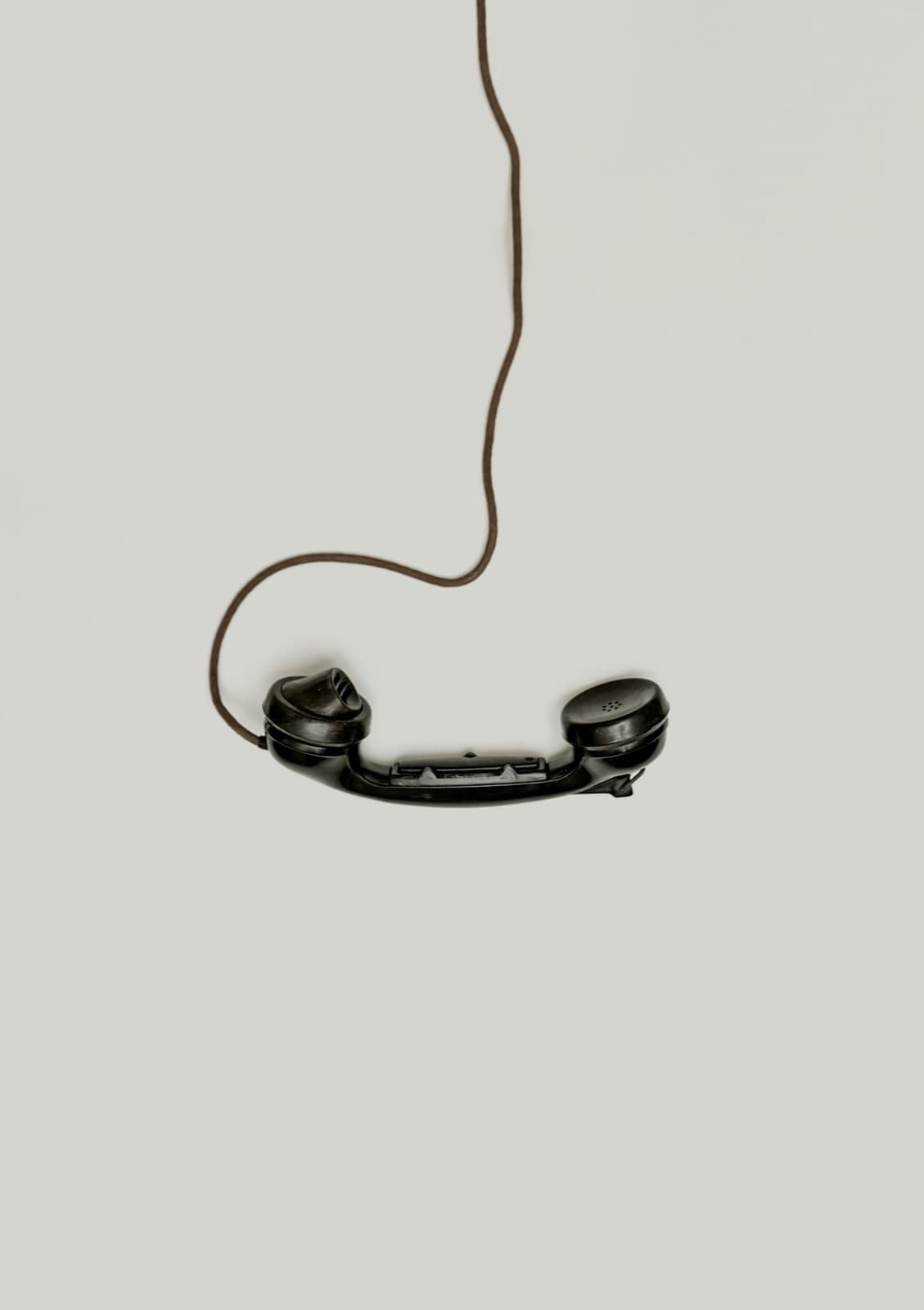 A black telephone handset hanging by its cord against a plain wall